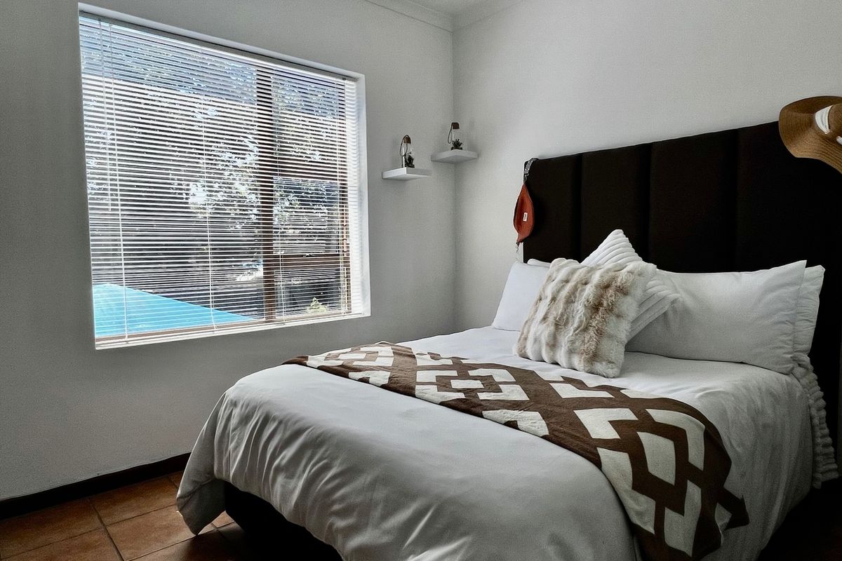 A well-lit bedroom featuring tiled flooring, floating wall shelves, and venetian blinds on the window.