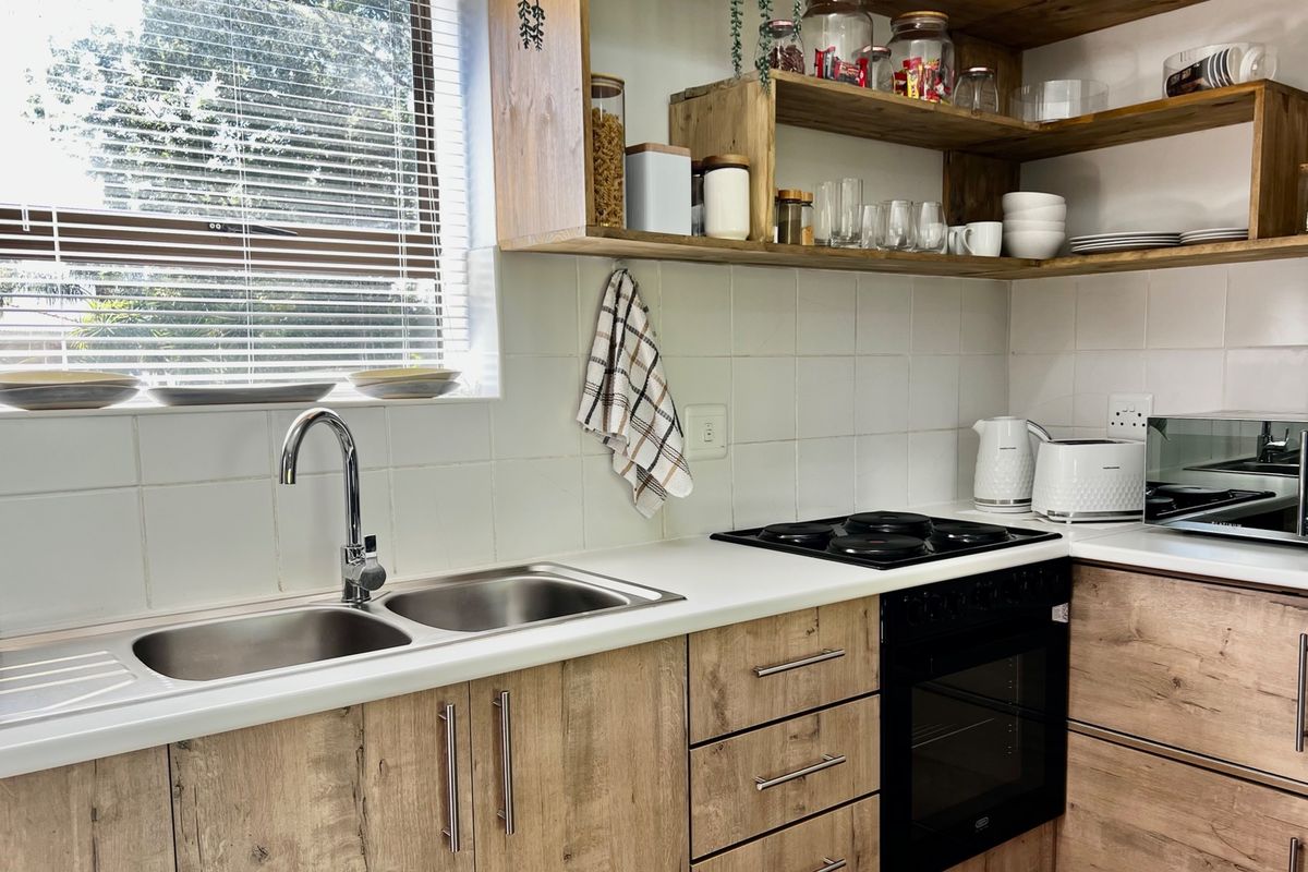 A well-maintained kitchen featuring wood-look laminate cabinetry, open timber shelving, a double bowl stainless steel sink, and a built-in electric oven with hob.