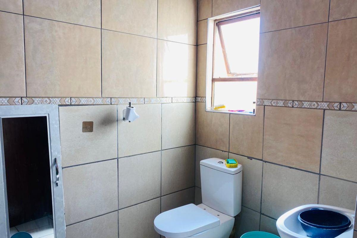 A functional bathroom featuring full-height ceramic wall tiles, a standard toilet, and a pedestal basin with a top-hung window for natural ventilation.
