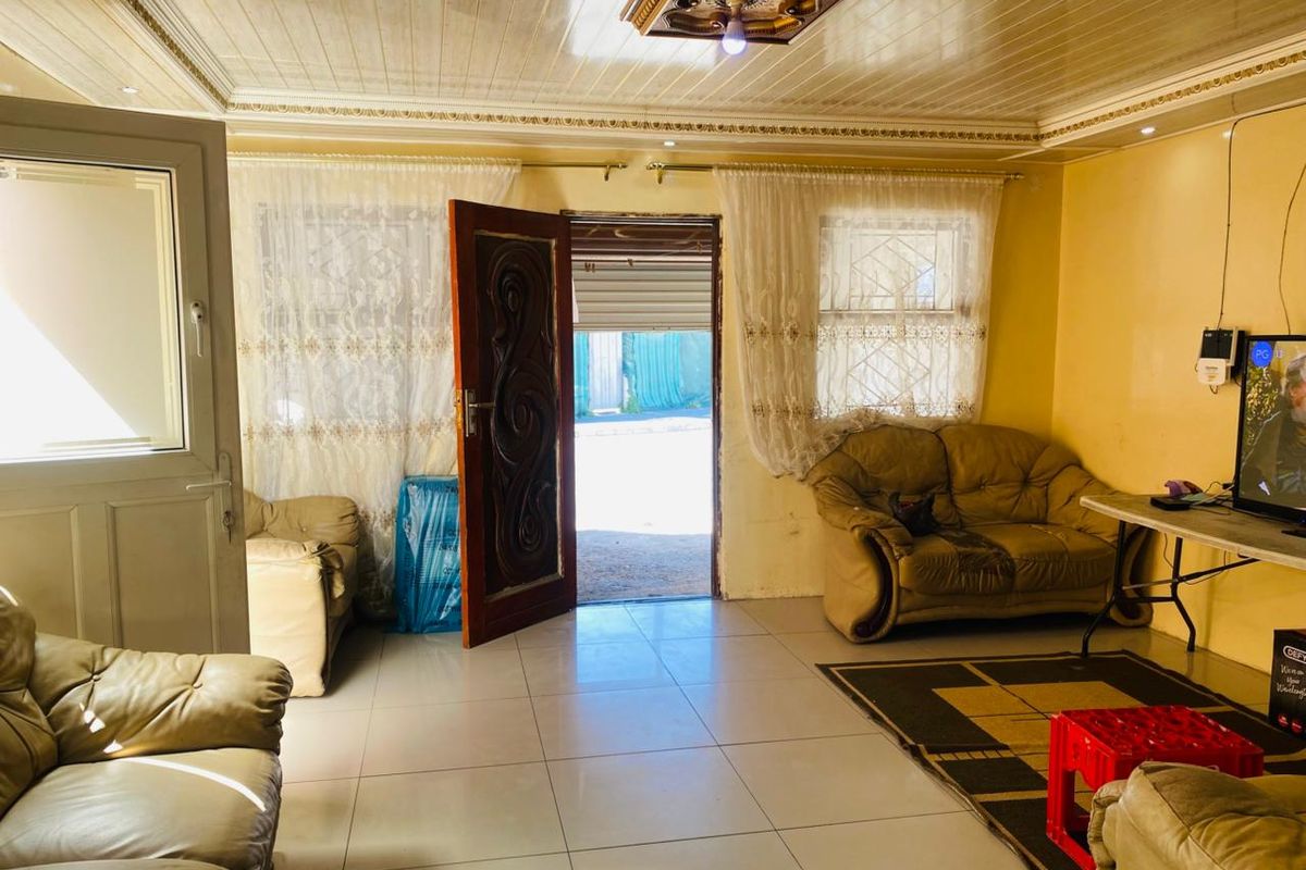 A living room featuring tiled flooring and decorative ceiling panels, with direct access to the exterior through a security door.
