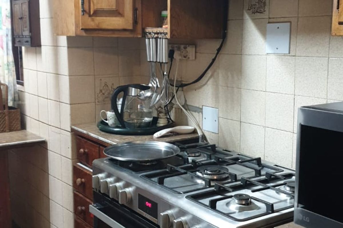 A dated kitchen featuring wooden cabinetry, a gas stove with an extractor fan, and tiled wall finishes.
