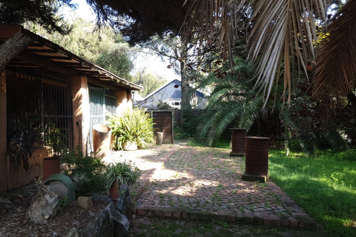 A rear garden area featuring a brick-paved patio, covered veranda, and mature landscaping, offering potential for outdoor renovation and improvement.