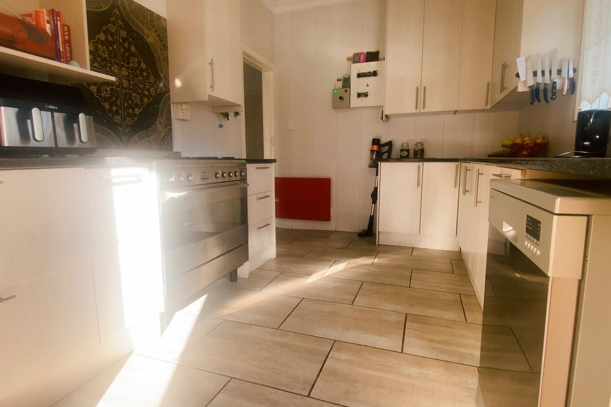 A functional kitchen featuring light-toned cabinetry, dark laminate countertops, stainless steel oven, and tiled flooring with ample natural light.