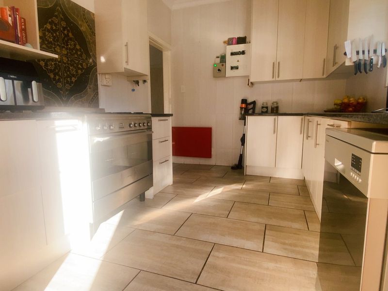 A functional kitchen featuring light-toned cabinetry, dark laminate countertops, stainless steel oven, and tiled flooring with ample natural light.