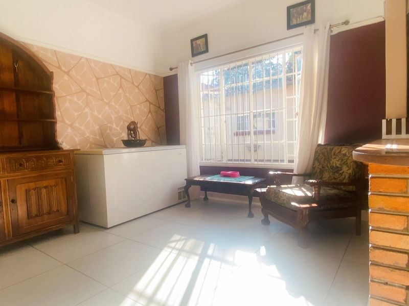 A living area featuring tiled flooring, a brick feature wall, and large windows fitted with security bars.