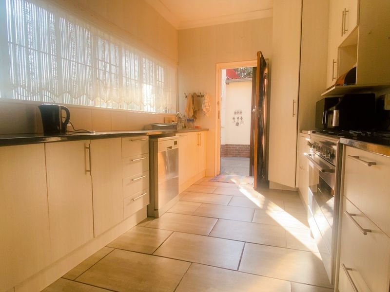 A functional kitchen featuring light-toned cabinetry, dark stone countertops, a gas hob, and tiled flooring with direct access to an outdoor area.