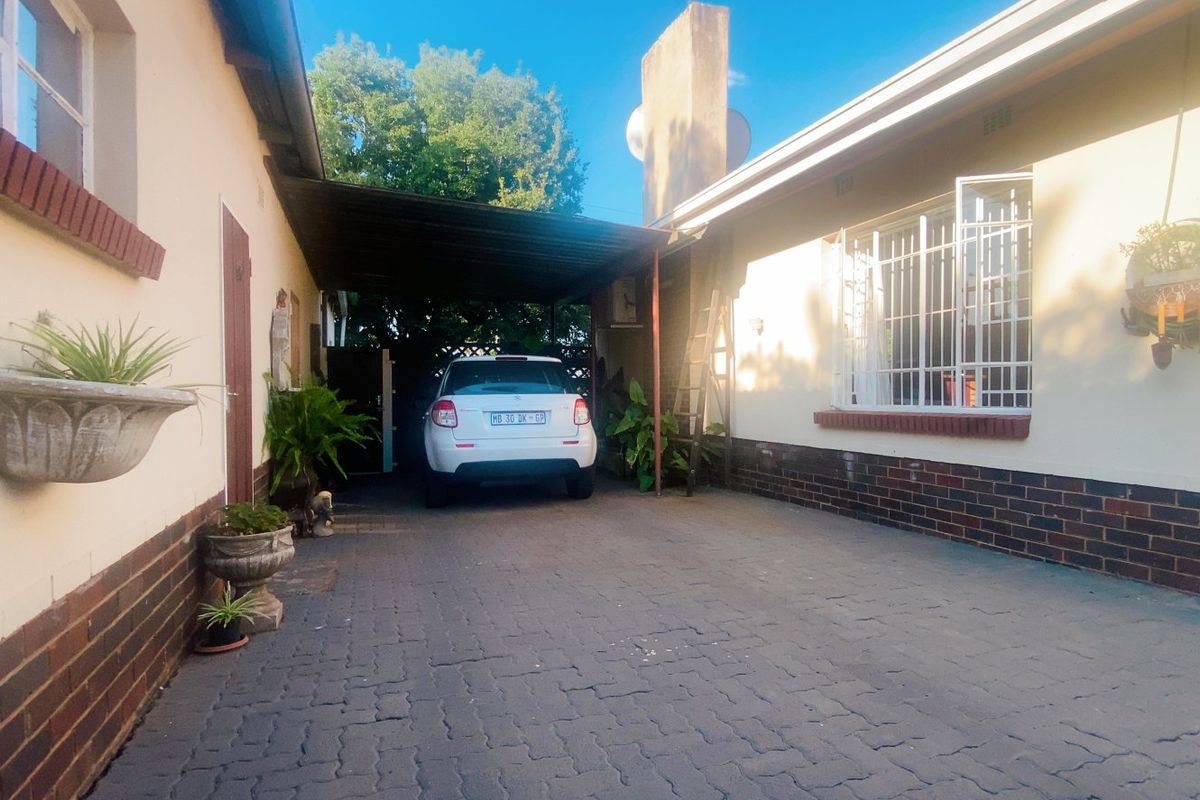 A paved rear driveway area featuring a covered carport structure and brick-accented exterior walls with security bars on the windows.