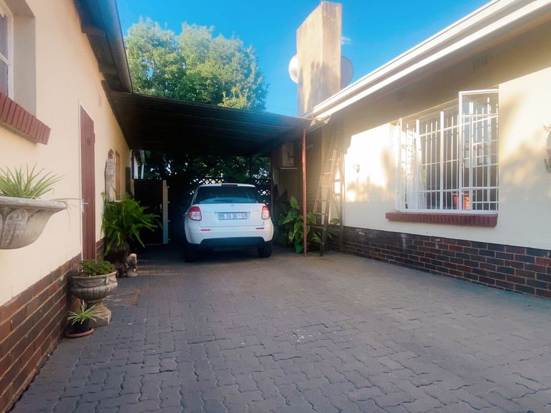 A paved rear driveway area featuring a covered carport structure and brick-accented exterior walls with security bars on the windows.