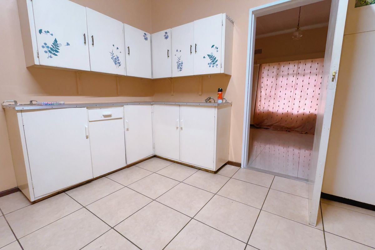 A functional kitchen area featuring white cabinetry, tiled flooring, and a doorway leading to an adjacent living space.