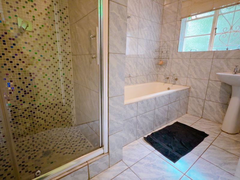 A functional bathroom featuring a glass-enclosed shower with mosaic tiling, a built-in bathtub, and a pedestal basin.