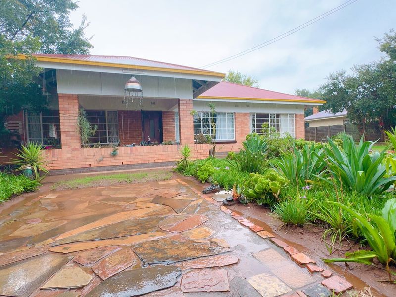 A charming single-story brick house featuring a covered front porch, metal roof, and a landscaped garden with a natural stone paved walkway.
