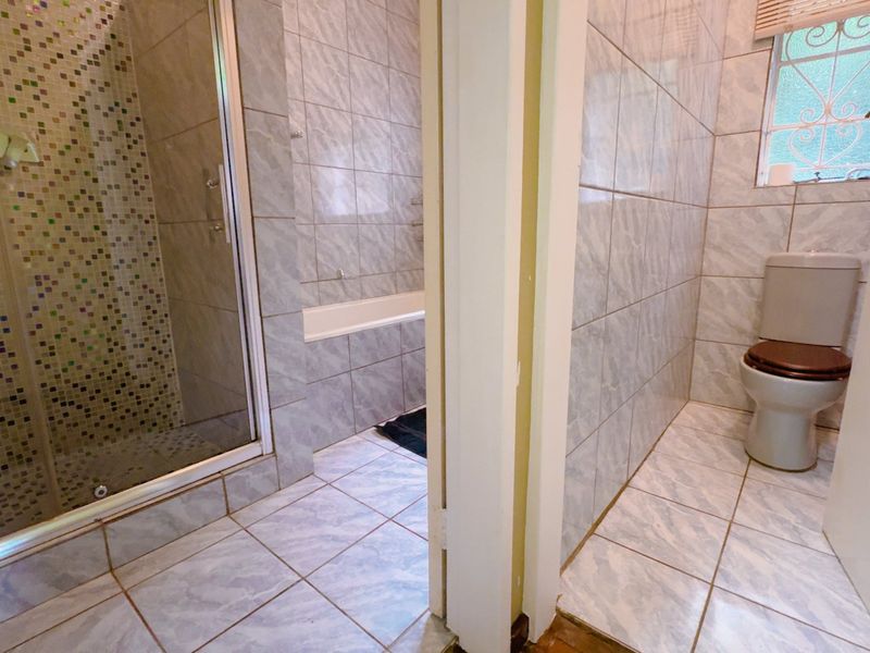 A functional bathroom featuring a separate shower cubicle with mosaic tiling, a built-in bathtub, and a private toilet area with a window.