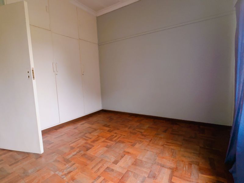 A bedroom featuring classic parquet flooring and built-in storage cupboards, offering a neutral canvas for personalization.