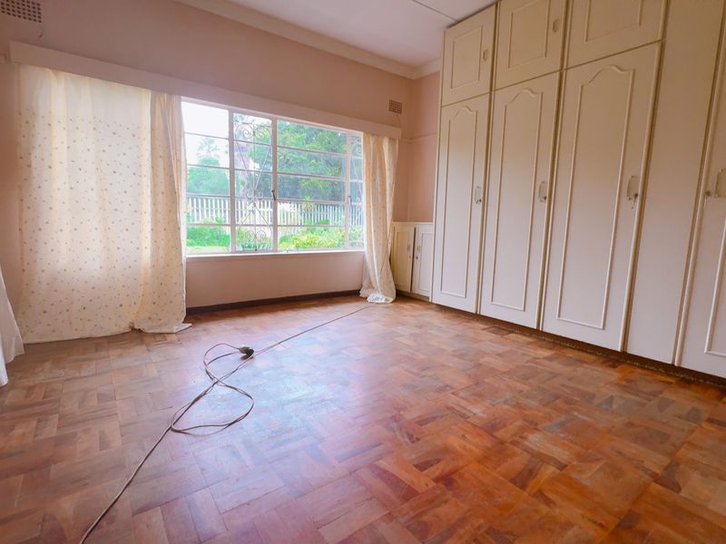 A spacious bedroom featuring classic parquet flooring, large windows for natural light, and extensive built-in cabinetry for storage.