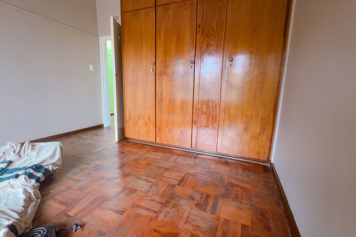 A bedroom featuring classic parquet flooring and built-in wooden cabinetry, offering a functional space with potential for modernization.
