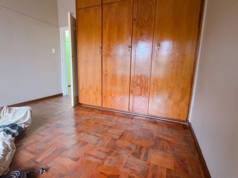 A bedroom featuring classic parquet flooring and built-in wooden cabinetry, offering a functional space with potential for modernization.
