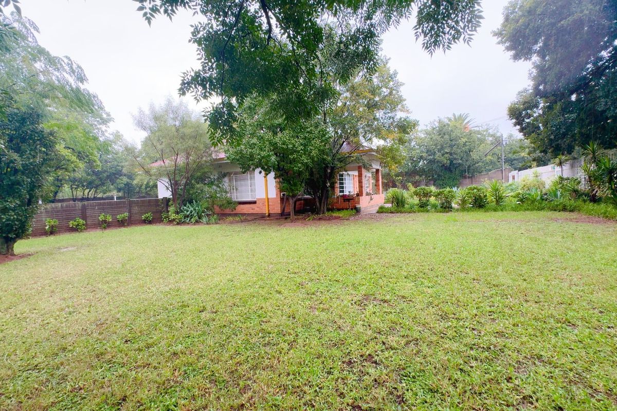 A spacious rear garden featuring a well-maintained lawn, mature trees, and a view of the back elevation of the house.