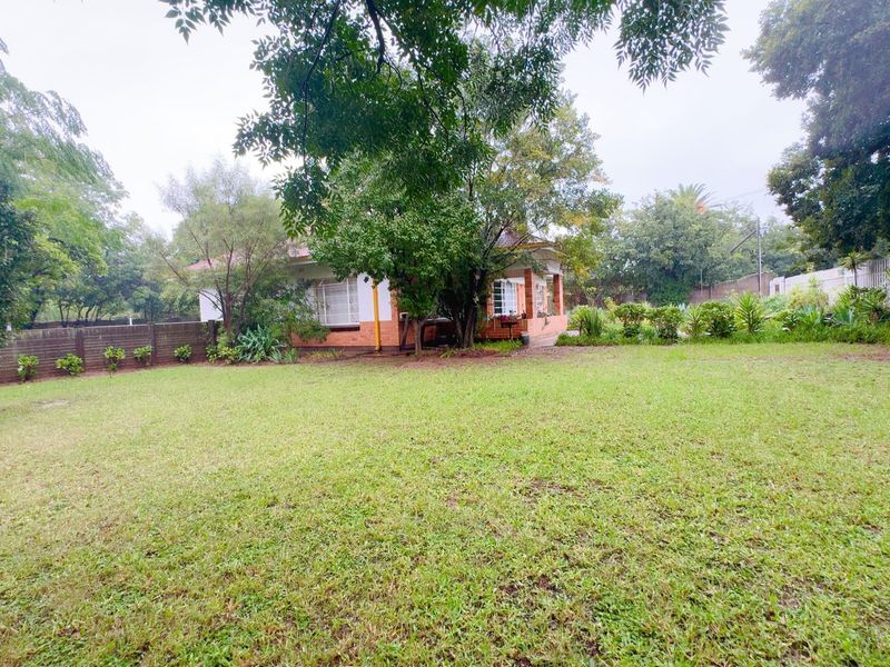 A spacious rear garden featuring a well-maintained lawn, mature trees, and a view of the back elevation of the house.