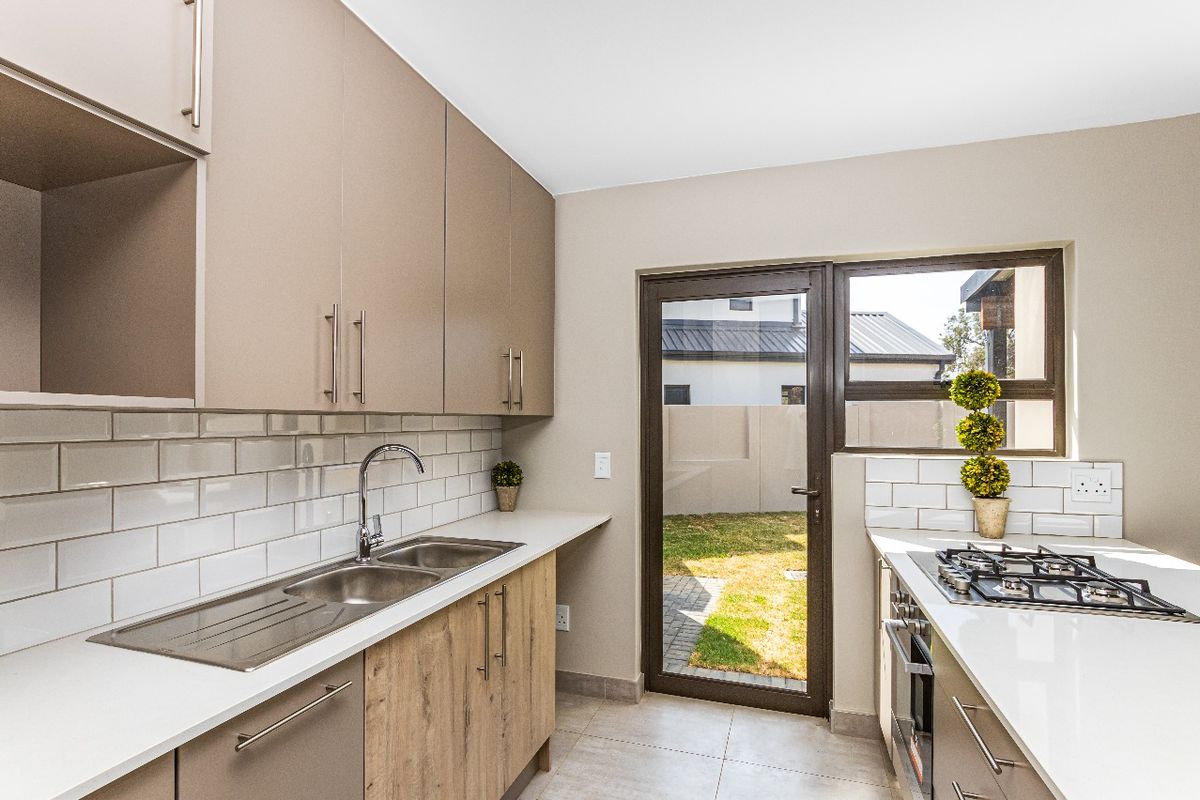 Modern kitchen featuring sleek cabinetry, stone countertops, subway tile backsplash, built-in gas hob, oven, and direct access to the rear garden.