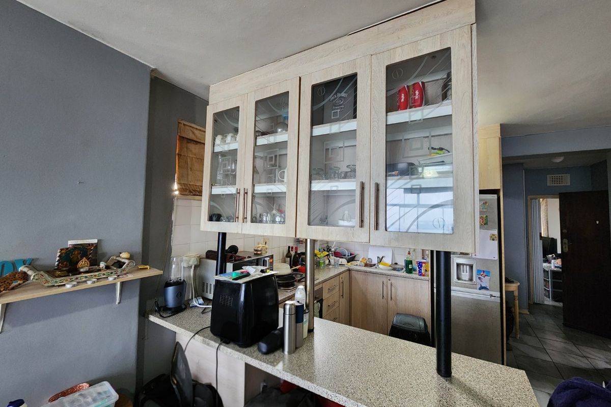 A functional kitchen area featuring overhead glass-fronted cabinetry, a breakfast bar, and laminate countertops with a tiled backsplash.