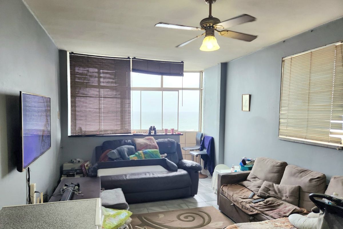 Living room featuring tiled flooring, a ceiling fan, and large windows with ocean views, requiring cosmetic updates to improve the overall aesthetic.
