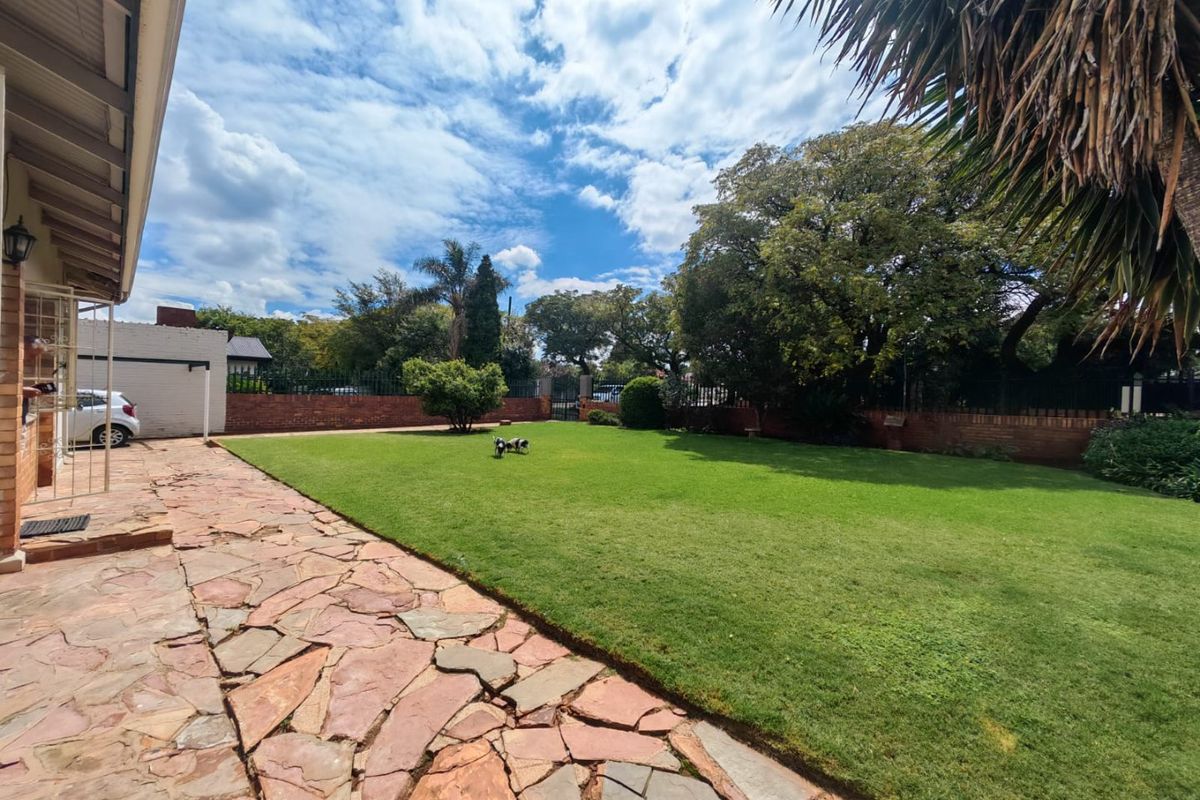 Spacious rear garden featuring a well-maintained lawn, flagstone paved patio area, and secure brick boundary walls.