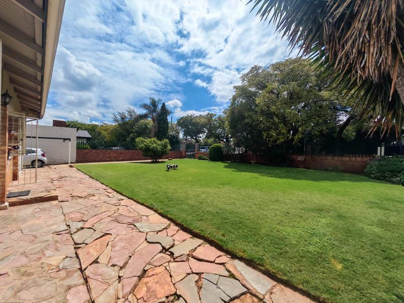 Spacious rear garden featuring a well-maintained lawn, flagstone paved patio area, and secure brick boundary walls.