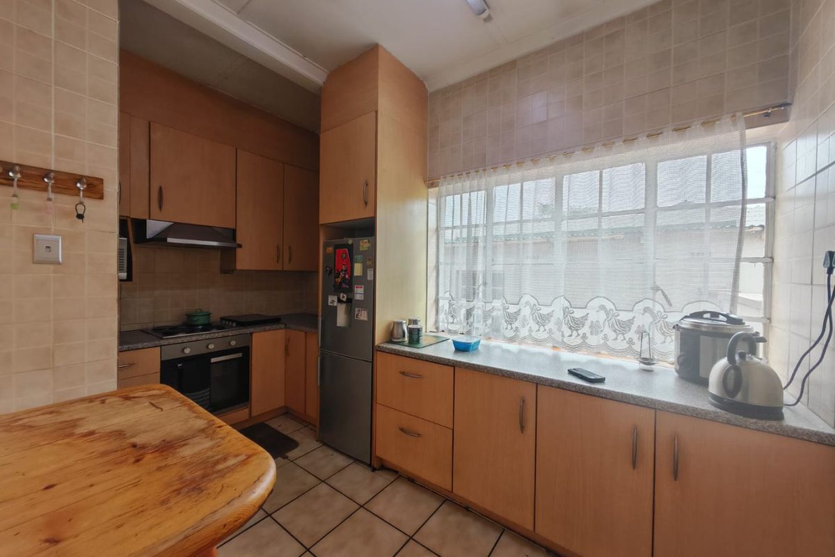 A functional kitchen featuring wood-look cabinetry, laminate countertops, built-in oven, hob, and extractor fan with tiled flooring and splashbacks.