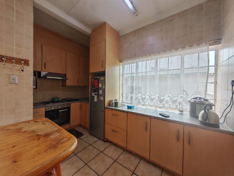 A functional kitchen featuring wood-look cabinetry, laminate countertops, built-in oven, hob, and extractor fan with tiled flooring and splashbacks.