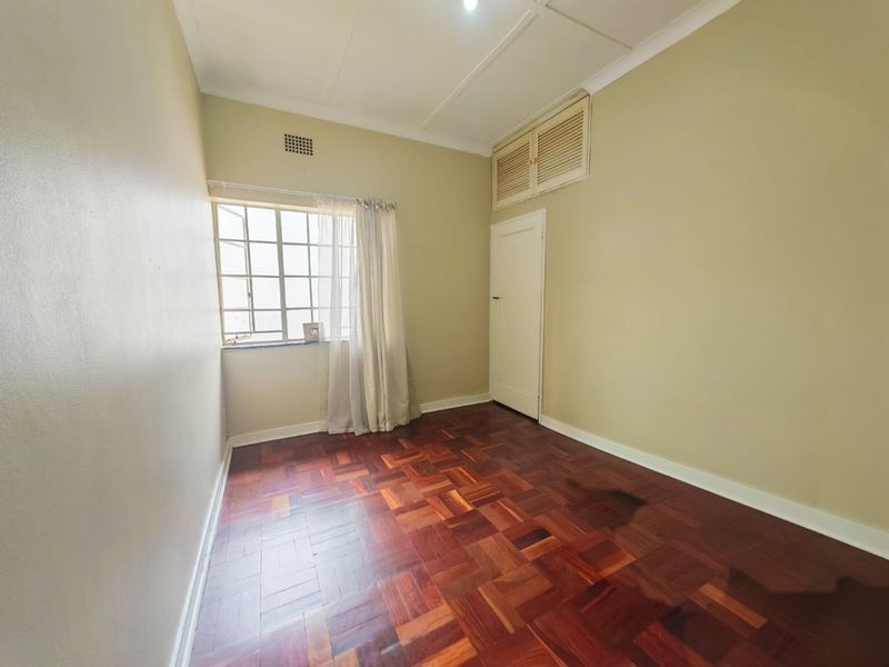 A vacant bedroom featuring classic parquet flooring, a built-in storage cupboard, and a steel-framed window, offering a neutral canvas for interior design.