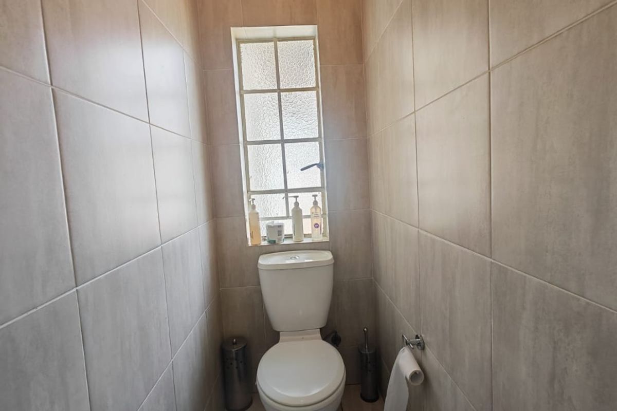 A compact, fully tiled guest toilet featuring neutral wall and floor tiles with a small obscured glass window for natural light.