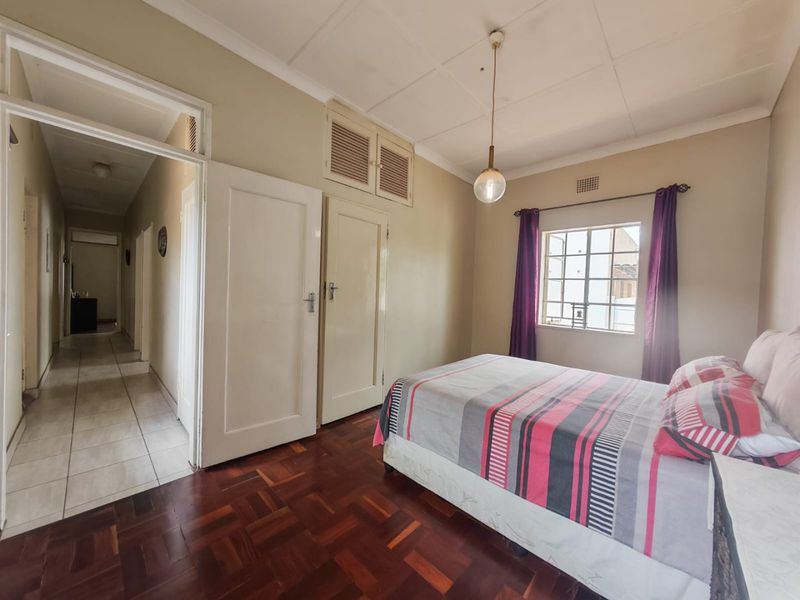 A bedroom featuring classic parquet flooring, built-in storage cupboards, and a window with natural light, providing a functional and well-proportioned living space.