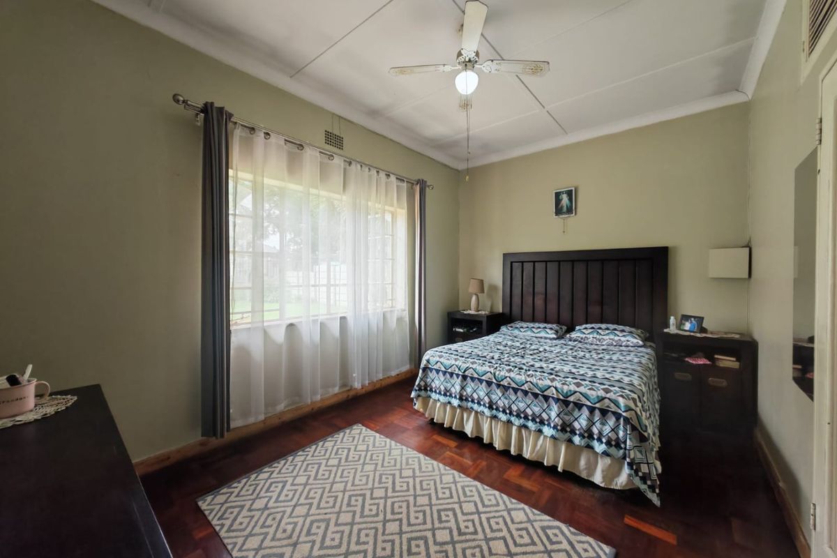 A well-proportioned bedroom featuring classic parquet flooring, a ceiling fan, and large windows that provide ample natural light.