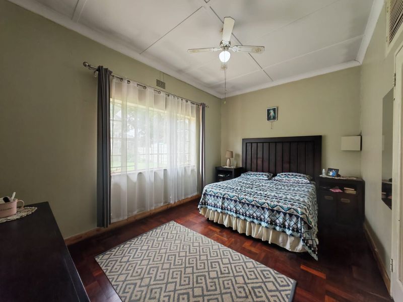 A well-proportioned bedroom featuring classic parquet flooring, a ceiling fan, and large windows that provide ample natural light.