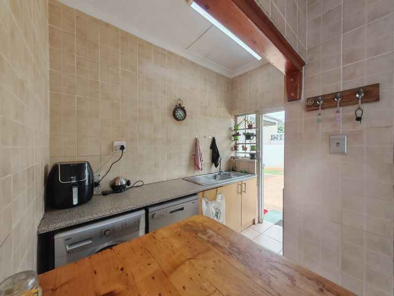 A functional scullery area featuring tiled walls, granite countertops, built-in cabinetry, and a stainless steel sink with direct access to the exterior.