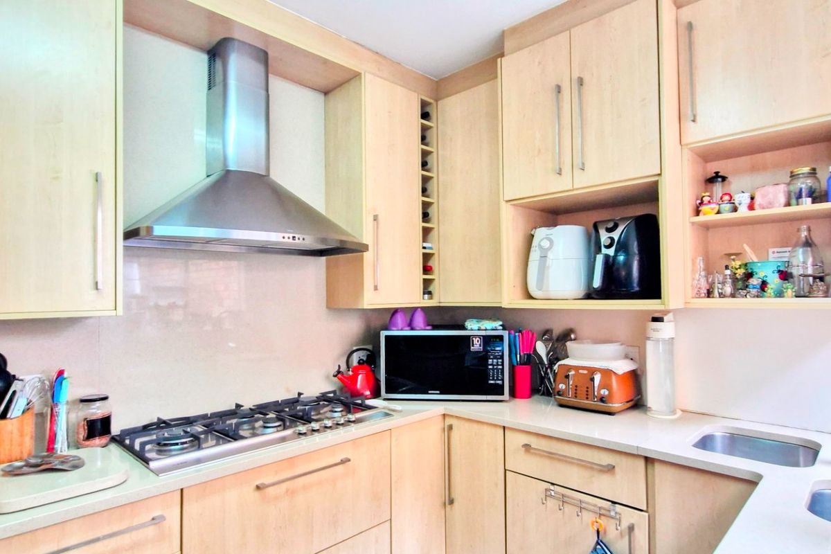 A functional kitchen featuring light wood cabinetry, stone countertops, a stainless steel gas hob, and an integrated extractor fan.