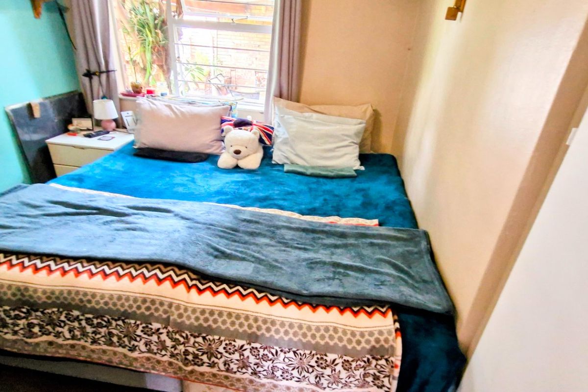 A compact bedroom featuring a window with security bars, providing natural light and a view of the exterior area.