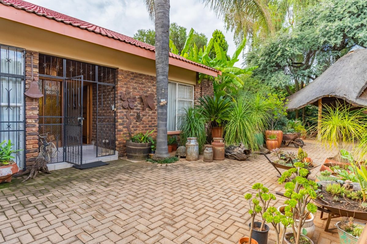 A rear exterior view featuring a brick facade, tiled roof, and a paved patio area with an adjacent thatched structure.