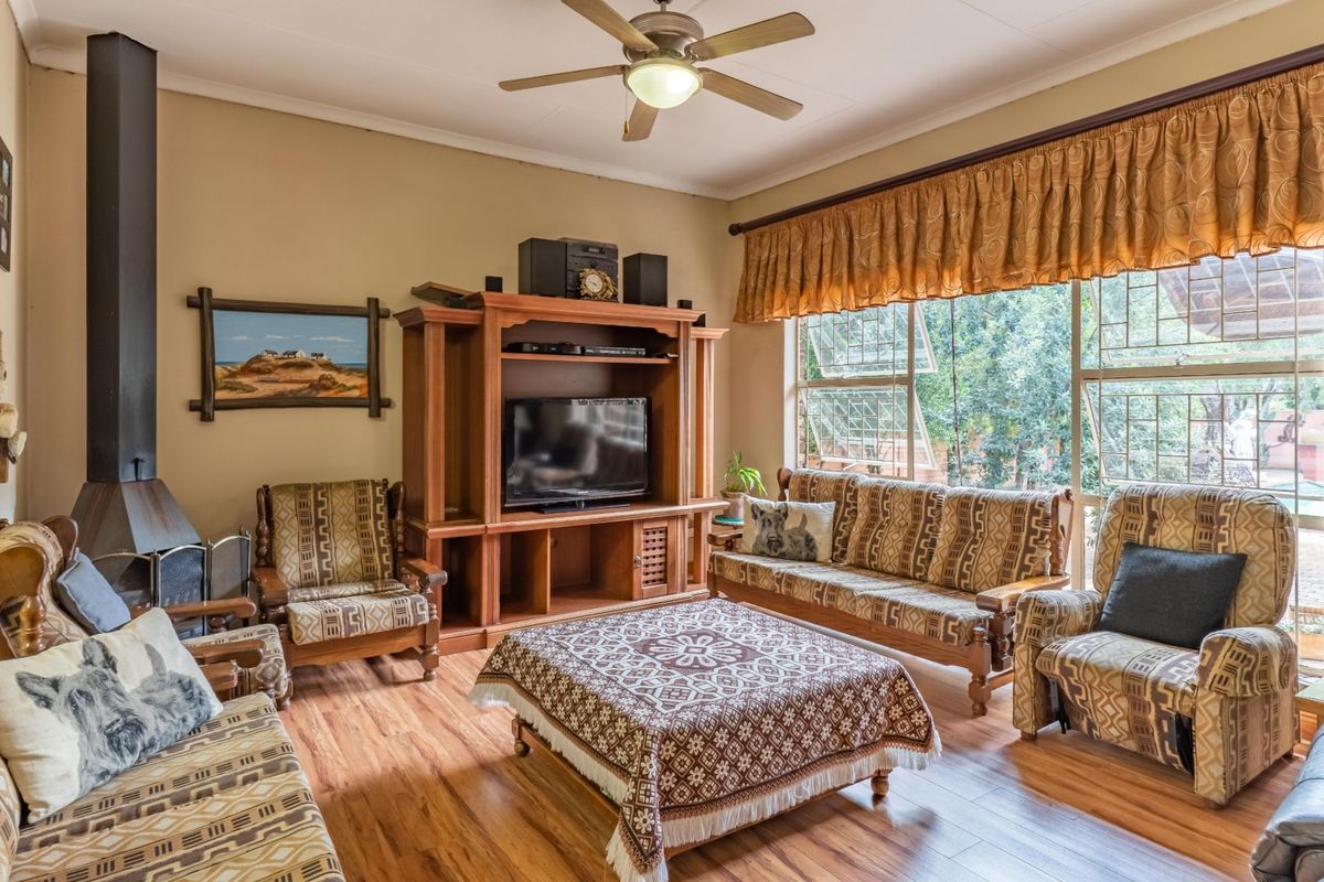 A comfortable living room featuring laminate flooring, a freestanding fireplace, and a large window providing natural light and garden views.