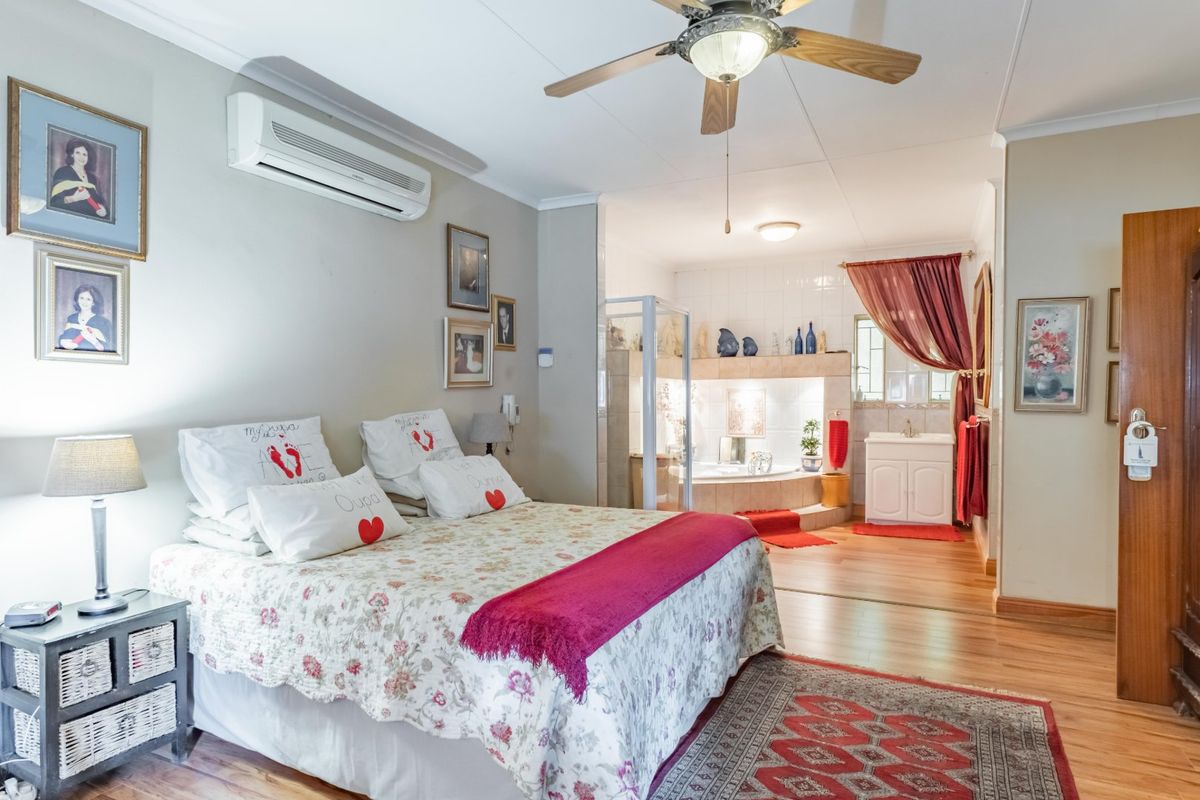 Spacious bedroom featuring laminate flooring, a ceiling fan, air conditioning, and an open-plan en-suite bathroom with a corner bathtub and shower.