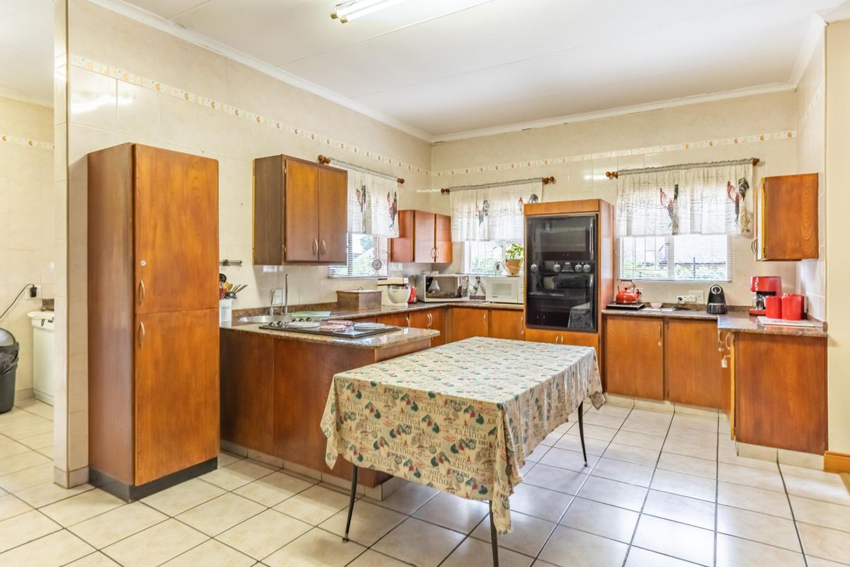A spacious kitchen featuring dated wooden cabinetry, granite countertops, built-in oven, hob, and tiled finishes throughout.
