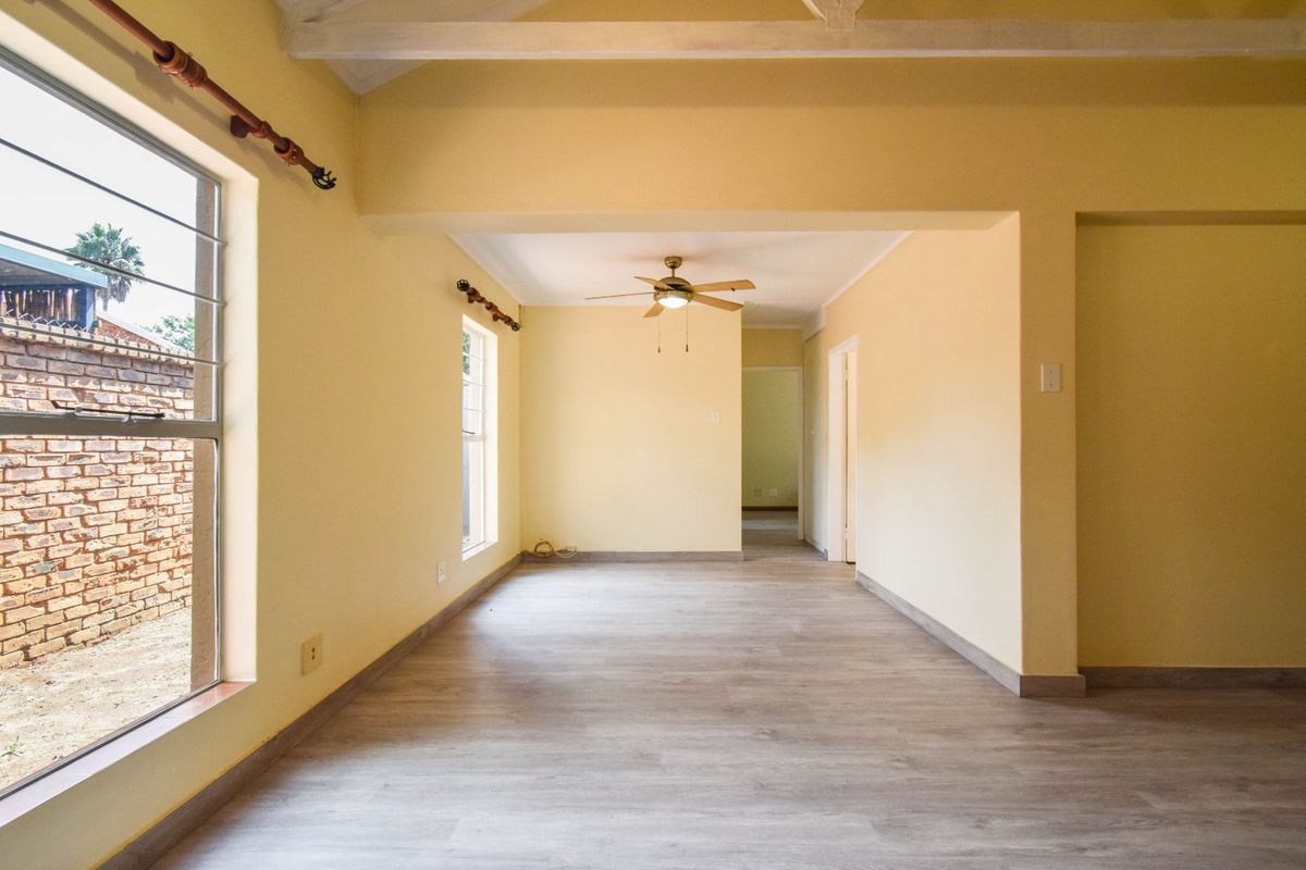 A bright, empty living area featuring modern laminate flooring, exposed ceiling beams, and a ceiling fan, offering a clean canvas for interior design.