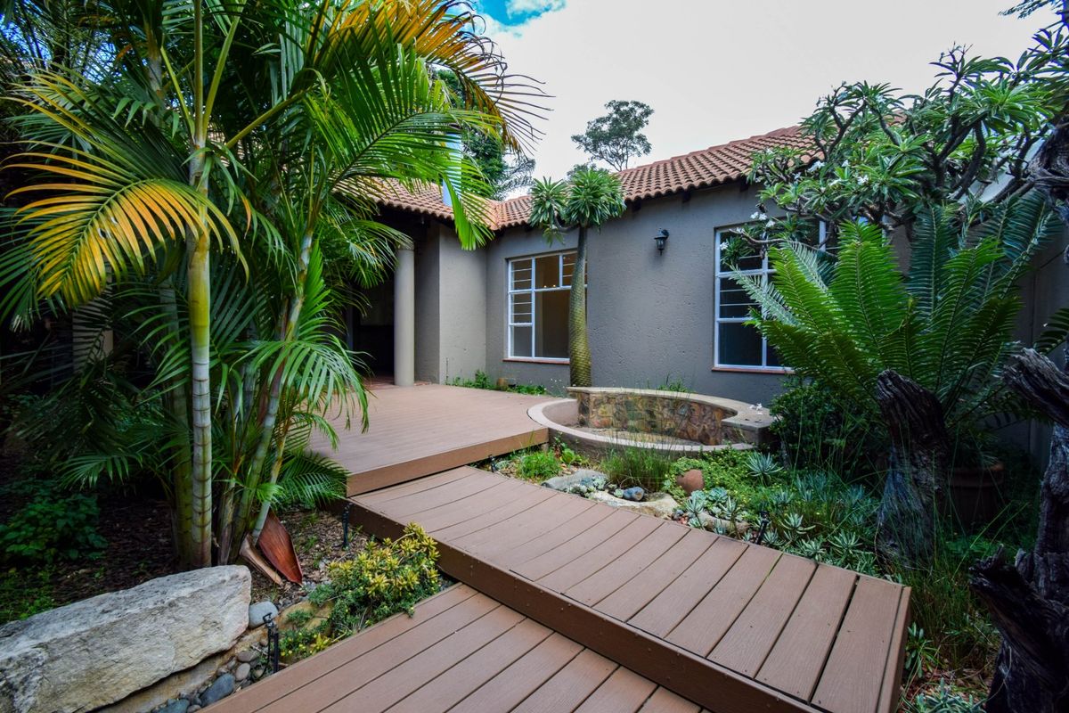 A well-maintained rear garden area featuring timber decking, a stone-clad water feature, and established landscaping against the house exterior.