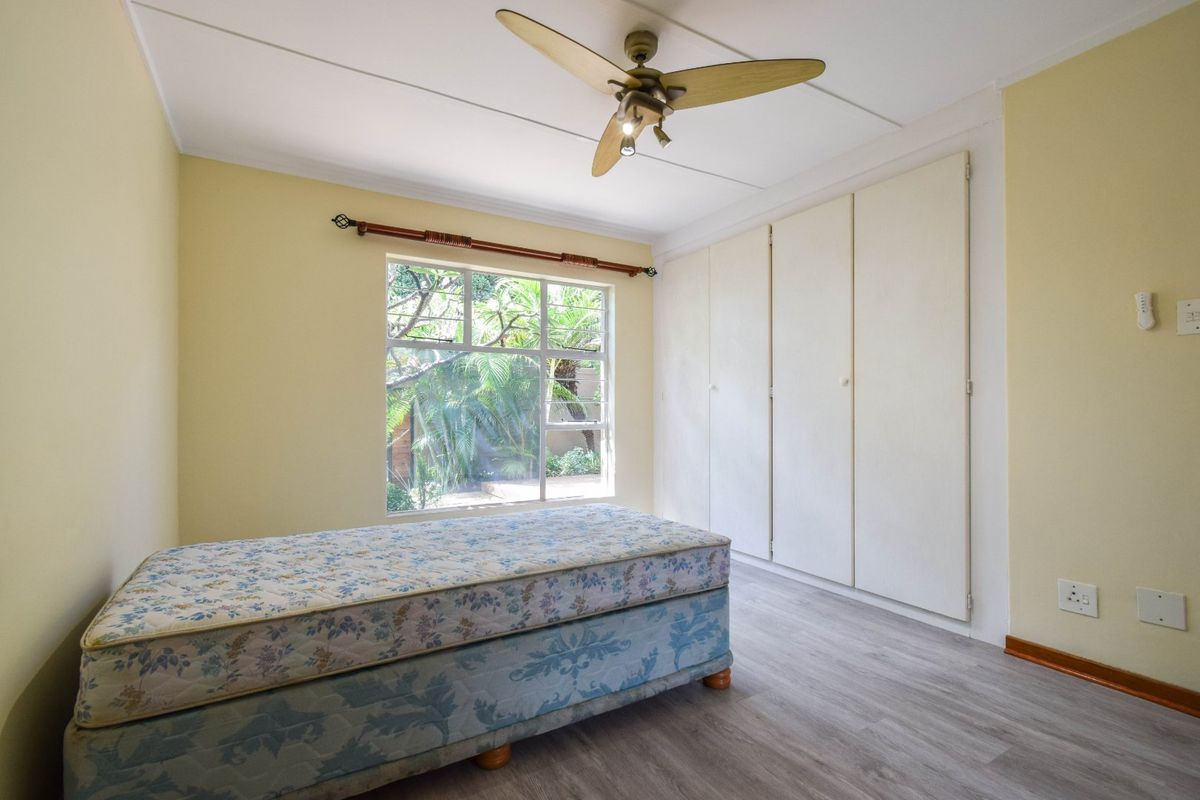 A bedroom featuring laminate flooring, built-in cupboards, and a ceiling fan, with natural light provided by a window overlooking the garden.