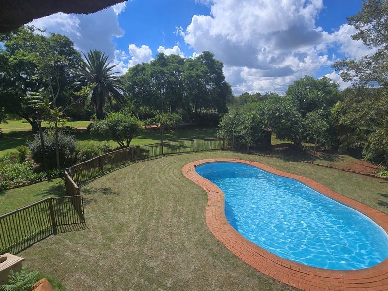 A well-maintained swimming pool with brick coping, surrounded by a landscaped garden and secure timber fencing on a spacious farm property.