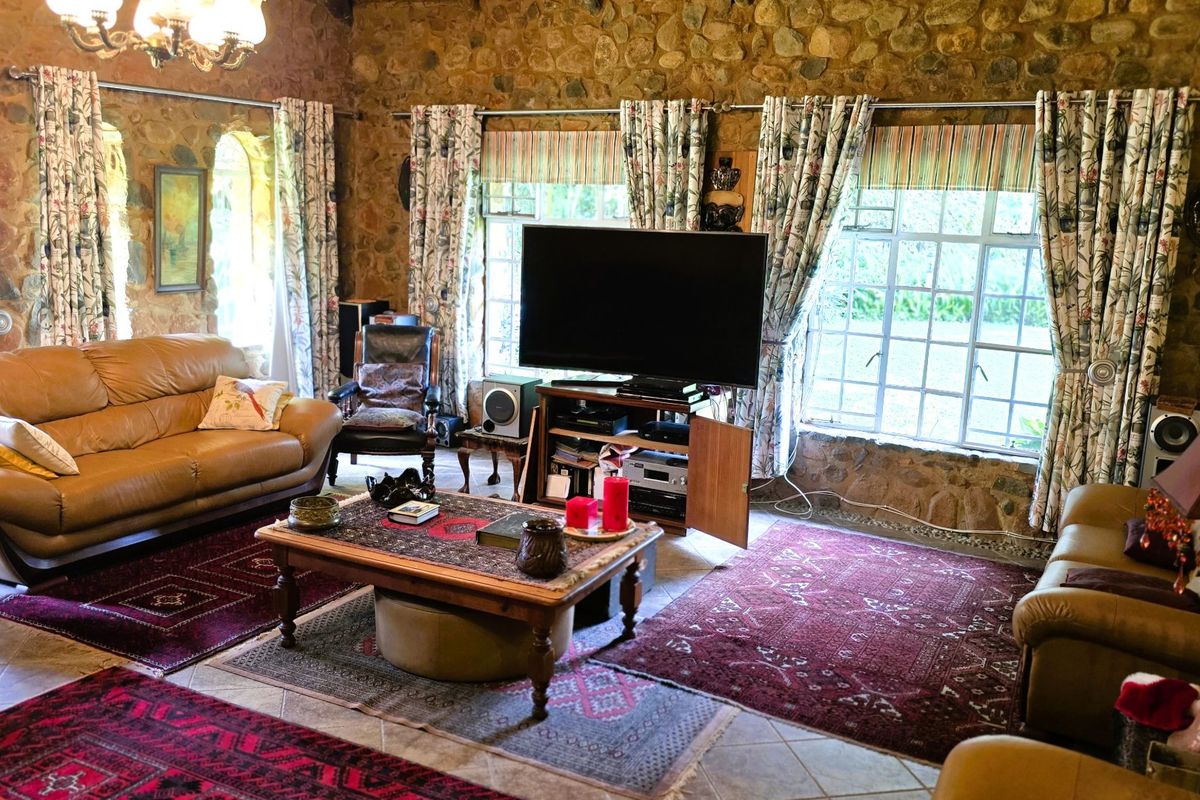 A rustic living room featuring distinctive stone masonry walls, tiled flooring, and large multi-pane windows that provide ample natural light.