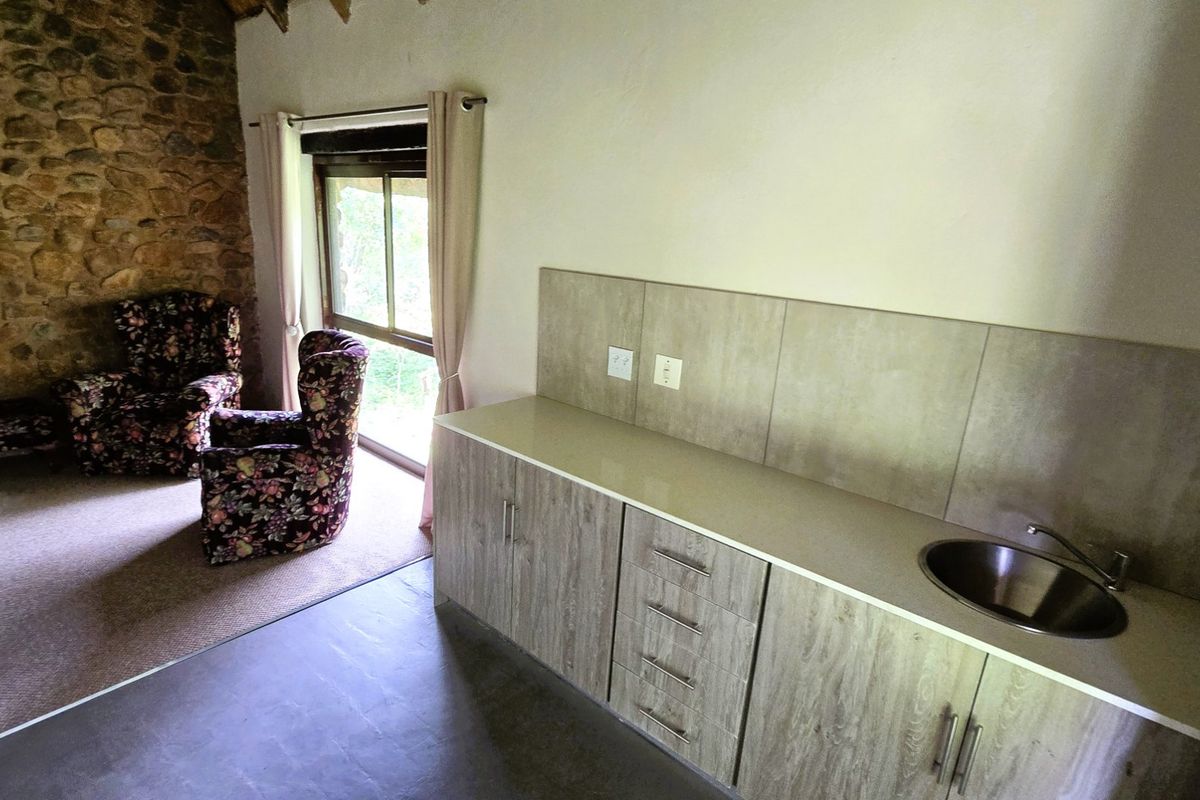 A kitchen area featuring wood-look cabinetry, a stainless steel sink, and a rustic stone feature wall, adjacent to a living space with garden access.