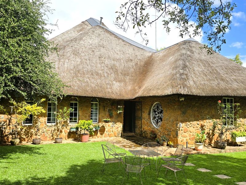 A charming farmhouse exterior featuring traditional thatch roofing, rustic stone wall cladding, and a well-maintained garden with a stone patio area.