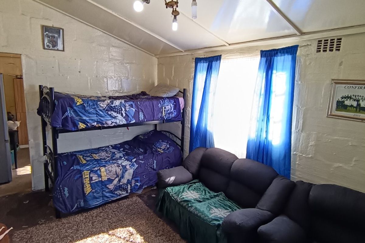 A bedroom featuring exposed blockwork walls, a sloped ceiling, and a central light fixture, offering potential for cosmetic updates and modernization.