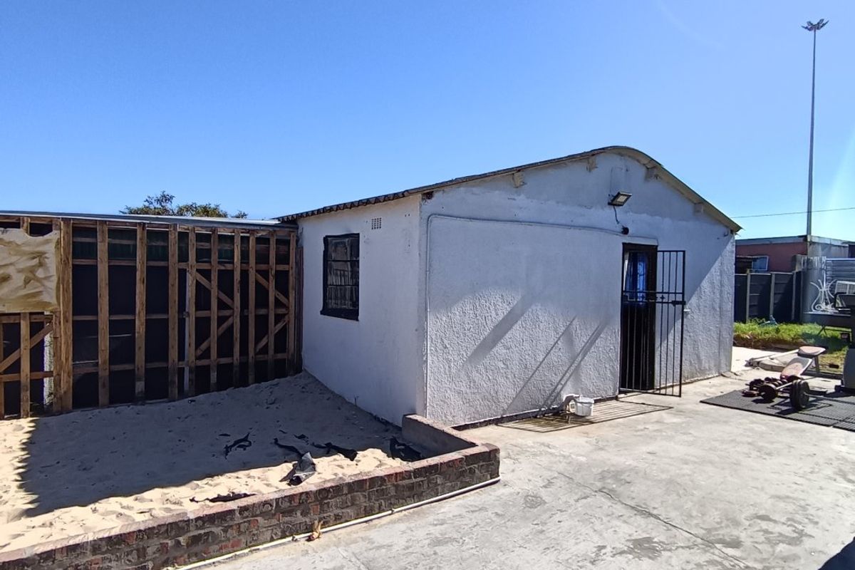Rear exterior view showing a concrete patio, brick retaining wall, and an unfinished timber frame structure attached to the main building.